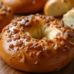A freshly baked onion bagel with a golden, crispy crust and savory onion topping, served on a wooden board with cream cheese on the side.