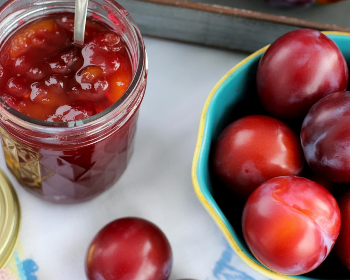 Homemade plum jelly recipe with fresh plums, sugar, and pectin cooking in a pot.